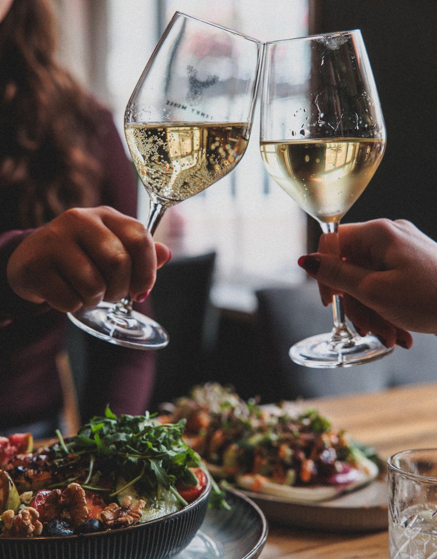 Twee wijnglazen proosten met elkaar boven een tafel vol eten.