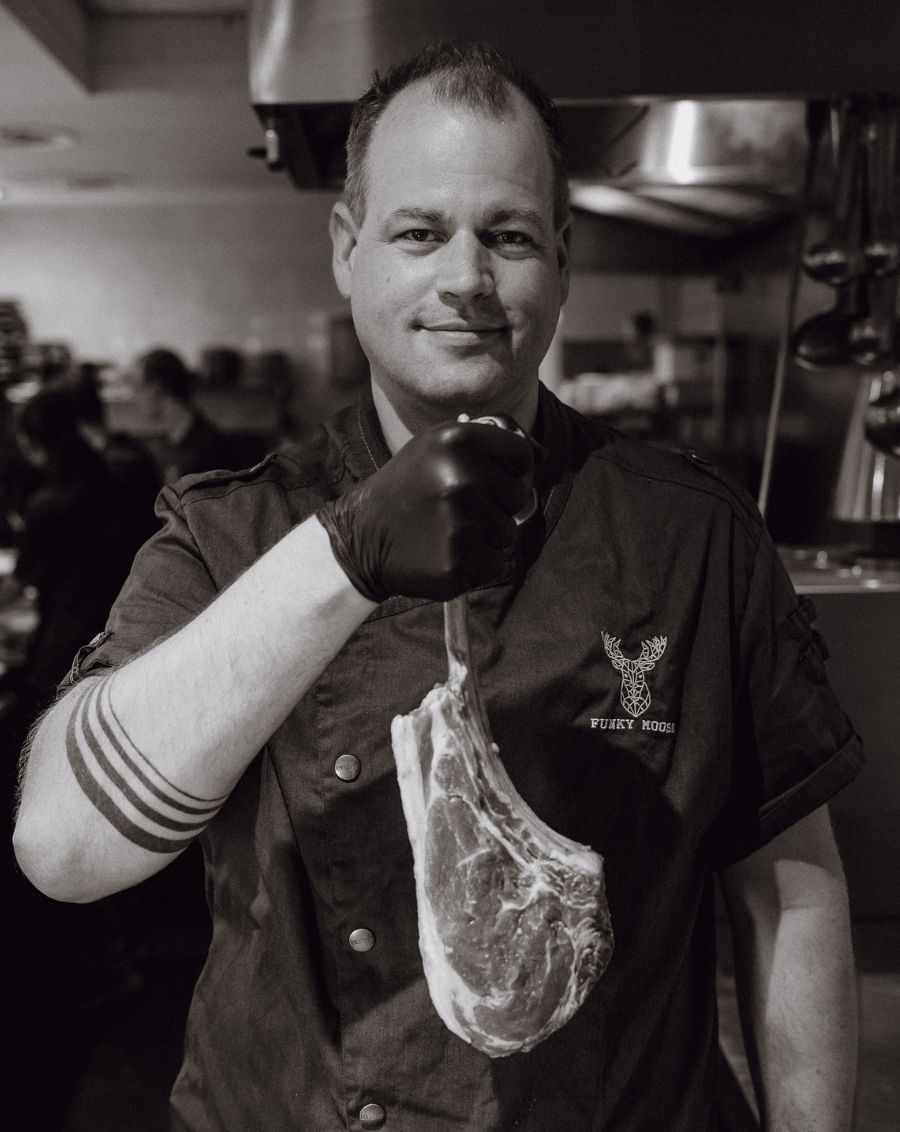 De chef kok en eigenaar staat met een grote Tomahawk steak
